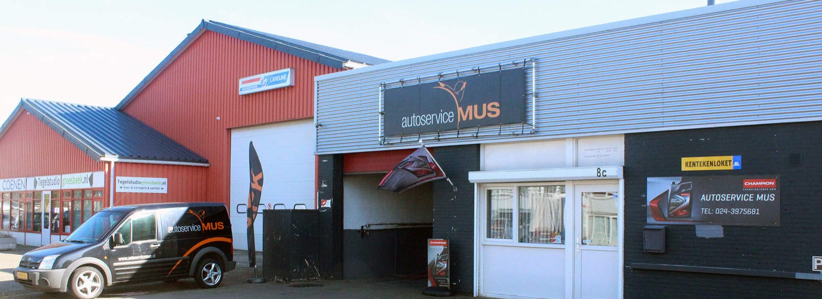 Het pand van Autoservice Mus met gevelbord, een geopende werkplaatsdeur en de bedrijfsbus ervoor